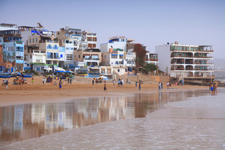 TAGHAZOUT, MOROCCO - FEBRUARY 27, 2022: People visit the beach in Taghazout surfing town near Agadir in Morocco.のeditorial素材