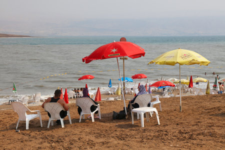 DEAD SEA, ISRAEL - OCTOBER 30, 2022: Tourists visit Dead Sea beach in Israel. Dead Sea is the lowest point on Earth, with famous dark mud believed to have therapeutic properties.のeditorial素材