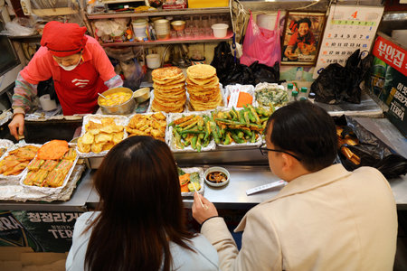 SEOUL, SOUTH KOREA - APRIL 7, 2023: People eat bindaetteok pancakes at Gwangjang Market in Jongno district of Seoul, South Korea.のeditorial素材