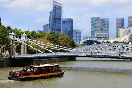 SINGAPORE CITY, SINGAPORE - MARCH 13, 2024: Tour boat on Singapore River approaching Cavenagh Bridge.のeditorial素材