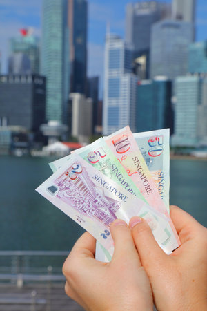 Hands holding Singapore dollars paper money with Singapore City skyline in background.の写真素材