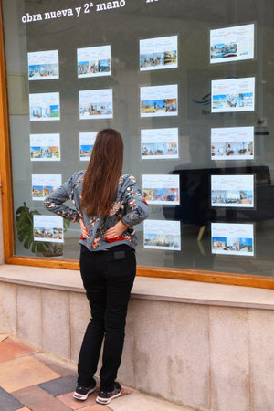 FINESTRAT, SPAIN - APRIL 12, 2025: Woman reads real estate ads in window display of a realty agency in Finestrat, Spain.のeditorial素材