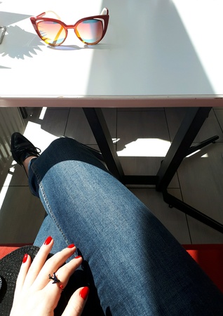 Stylish lady sitting in a cafe wearing jeans, with red finger nailsの素材