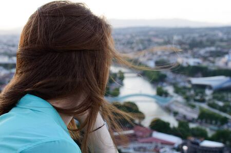 Close view of a red-haired tourist girl looking at a defocused panorama of a modern cityの写真素材