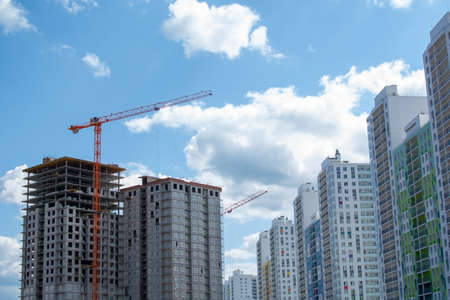 A multi-storey building under construction against the new bright finished residential buildings. High-rise cranes for the construction of new apartment buildings. Houses for purchase with a mortgage.の写真素材