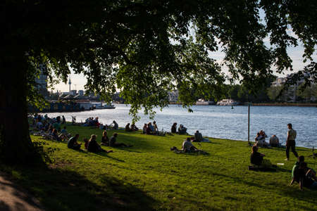 Berlin, Germany - Jun 21 2020 : People sitting on grass near sunset at the Spree river side.