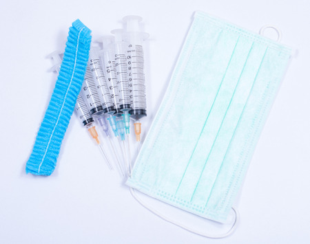 Surgical glove, mask, cap and syringe on white background.