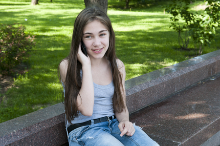 Young attractive girl speak to phone on bench. Summer park. Smile. Photoの写真素材