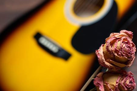 Acoustic guitar with dried roses on the wooden table. Template for advertising a concert of memory...
