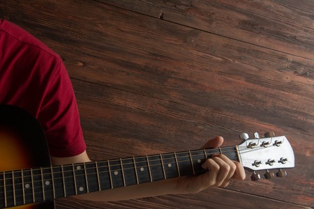 Hand of man playing six string guitar on wooden background