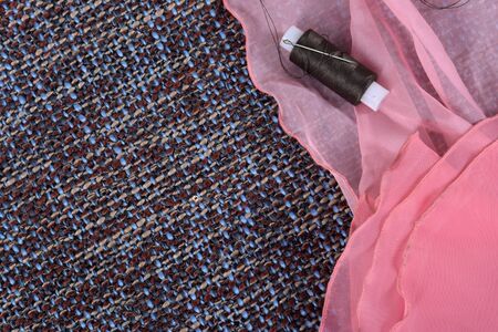 Pink silk fabric and bobbin threads on a gray background