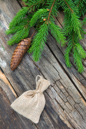 Small bag of burlap and branch green spruce with cone background of a wooden old tableの写真素材