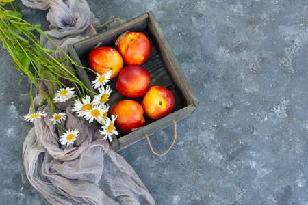 Bouquet of wild flowers chamomile with fruits of nectarines in a wooden boxの写真素材