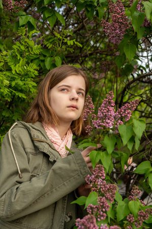 Portrait of a young teenage girl in the garden, a bush of blooming lilacs in the spring.の写真素材