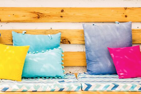 Close up pillows on an outdoor patio chair, with a blue striped cushioned bench.の写真素材