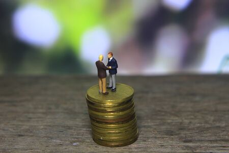 Simple Illustration Photo Successfull Bussiness Transaction, Two Man Handshaking at golden indonesia 500 Rupiah Coin, Green Forest as a backgroundの写真素材
