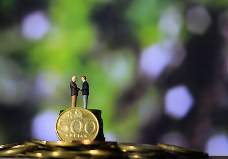 Simple Illustration Photo Successfull Bussiness Transaction, Two Man Handshaking at golden indonesia 500 Rupiah Coin, Green Forest as a backgroundの写真素材