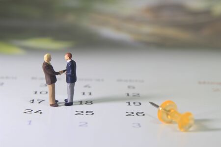 Simple Illustration Photo, Two Man Handshaking, Business Agreement at Calendar beside transparent yellow push pinの写真素材