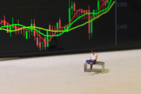 Conceptual Photo, illustration for Young Man Investor Mini Figure Toy businessman Seriously watching Running Stock Exchange Sitting at stapplerの写真素材