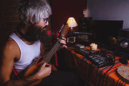 Portrait of bearded man men's jacket barefoot whit acustic guitars sitting of a bed