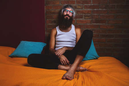Portrait of bearded man men's jacket barefoot whit acustic guitars sitting of a bed