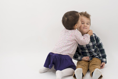 little girl kissing her older brother on the cheek isolatedの写真素材