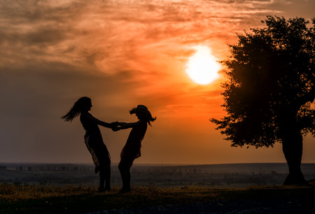 silhouette of two women dancing on the grass at sunset timeの写真素材