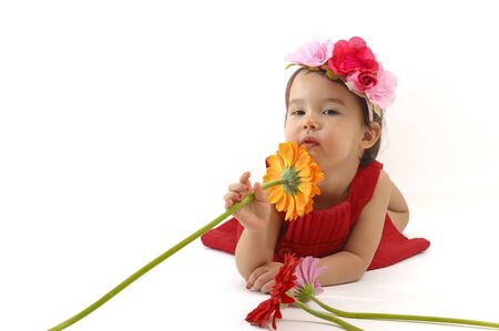 little girl in red dress smelling a gerbera flowerの写真素材