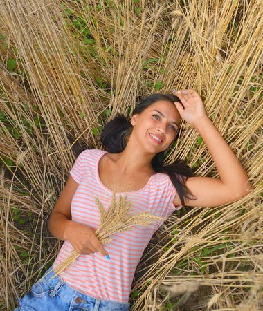 Cute dreamy girl on golden ripe wheat field, lying downの写真素材