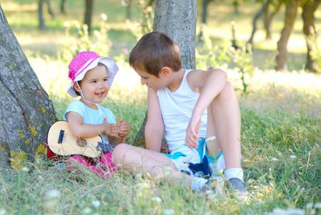 boy and his younger sister play guitar and sing in gardenの写真素材