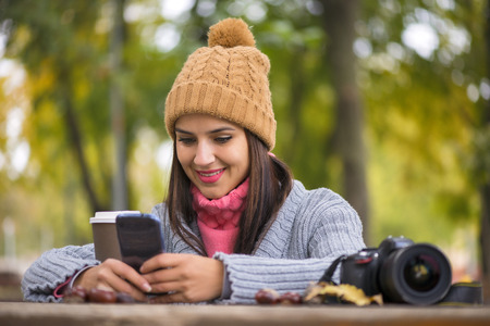 Beautiful girl messaging with phone in autumn parkの写真素材