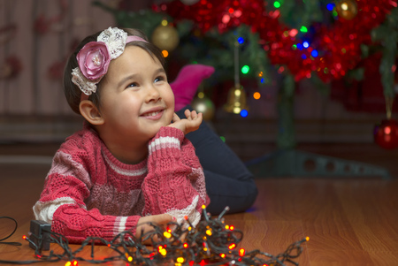 Portrait of cute little girl with Christmas tree on backgroundの写真素材