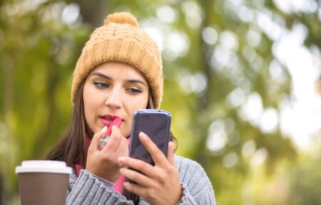 Woman making make-up, applying lipstick looking at the phone like in a mirrorの写真素材
