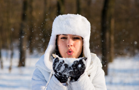 Girl in the park in winter blowing snowflakes