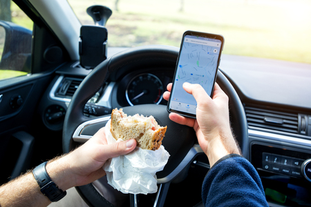 man eating and texting while driving carの写真素材