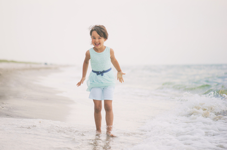 Little girl with blue dress having fun in sea waterの写真素材