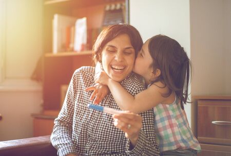 Mother enjoying with her daughter while looking at the positive pregnancy test
