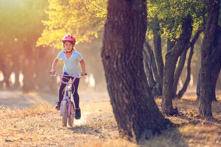 Little girl having fun on bike in the forest in autumn seasonの写真素材