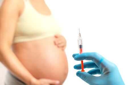 Doctor hand preparing to injects anticoagulants into pregnant woman belly, isolated on white backgroundの写真素材