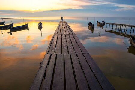 beautiful sunrise over water and silhouette of fishing boatの写真素材