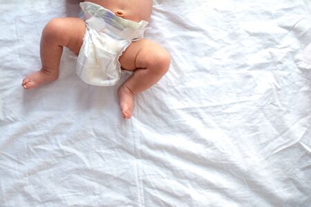 Baby legs and bottom in diaper on white bed background, top view, copy space