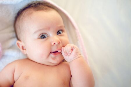 Portrait of a little newborn girl who has her  finger in mouth