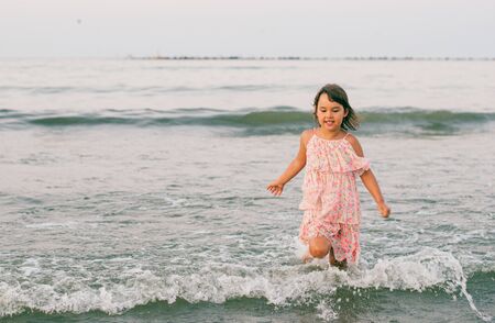 Little girl with pink dress having fun in sea water