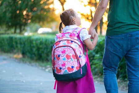first day at school. father leads a little child school girl in first grade