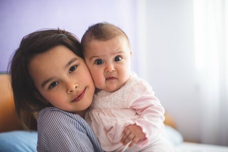 Big little sister holding her little sister and looking at camera with funny faces