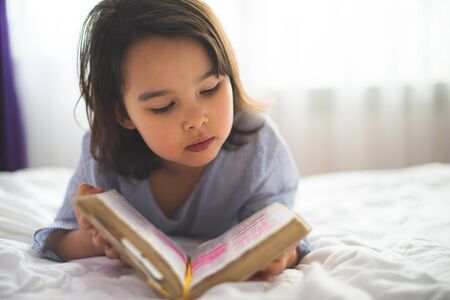Little girl reading from bible while she is in bed in the morningの写真素材