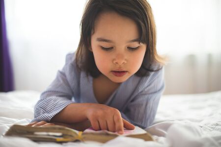 Little girl reading from bible while she is in bed in the morningの写真素材