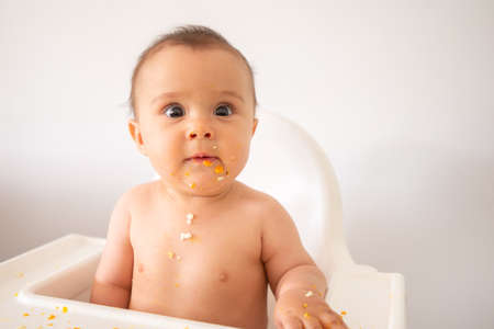 A funny adorable and dirty little baby girl of 6 months eats while sitting in the baby chair.