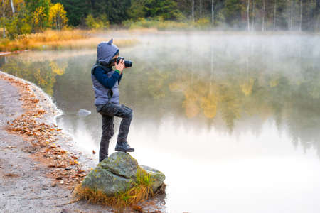 Creative child, kid photographer (a little boy) with a camera taking landscape pictures near la lake