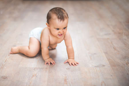 Small adorable infant standing on all fours on wooden floor at home.の写真素材
